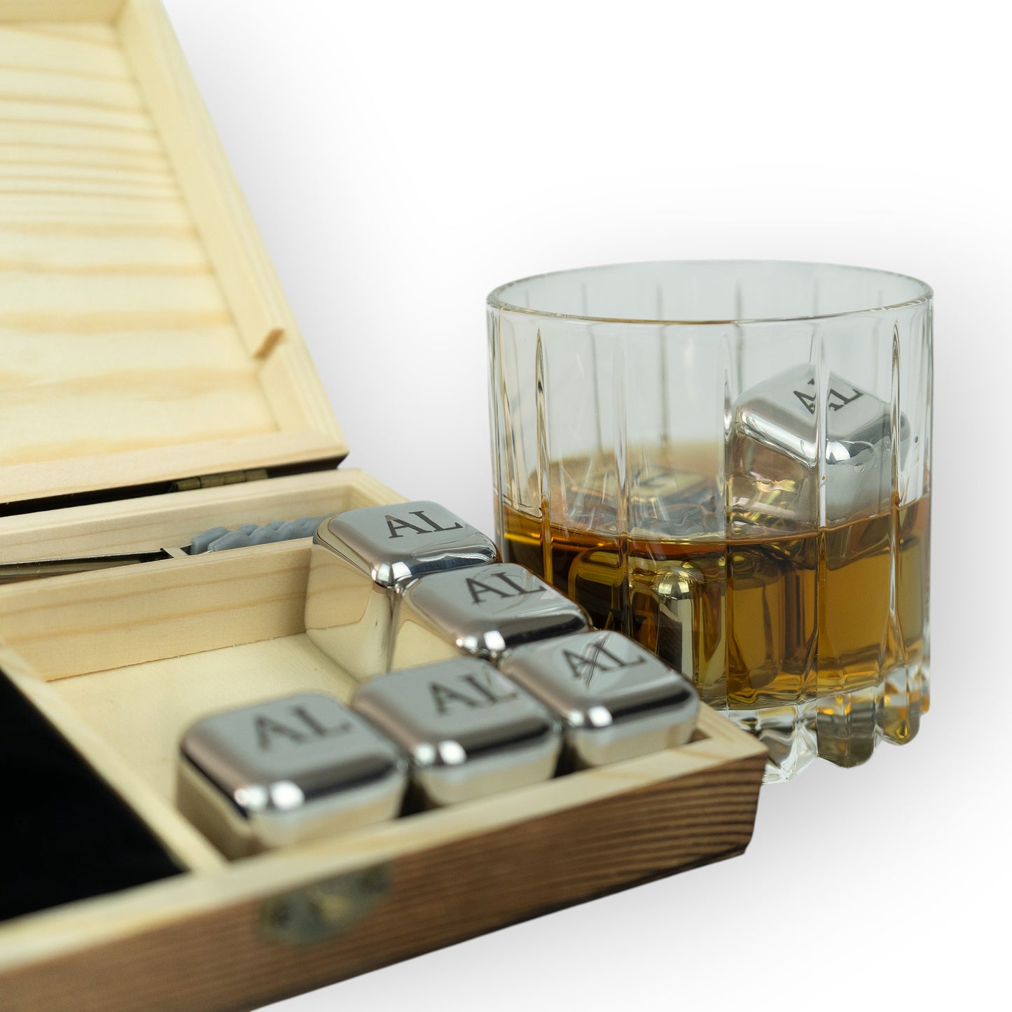 HouseEco personalised stainless steel whiskey stones with 'AL' engraving in a wooden box, one stone in a glass of whiskey.