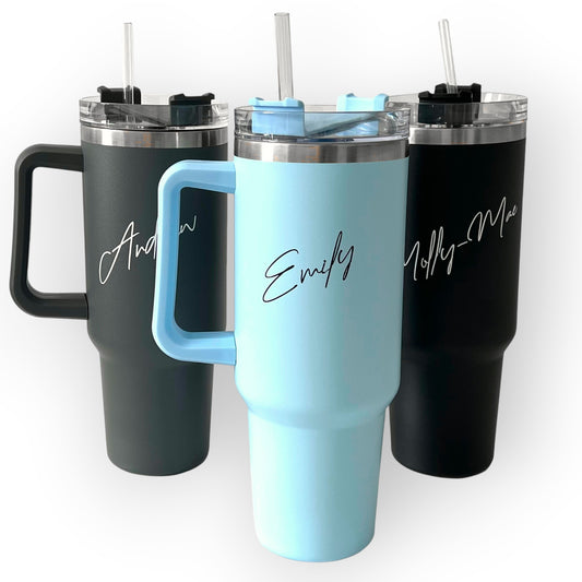 HouseEco personalised 1.2L insulated travel mug with handle and straw in black, light blue, and dark grey. Features custom name engraving.